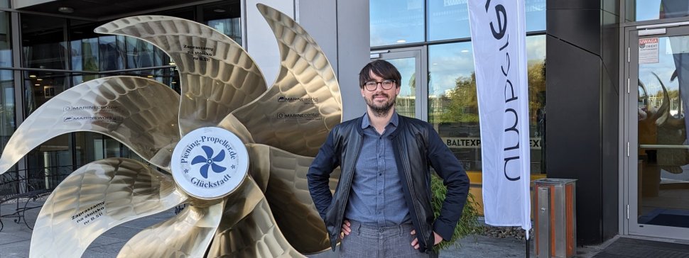 Professor Grzegorz Liśkiewicz in front of the entrance to the building, standing next to the sculpture