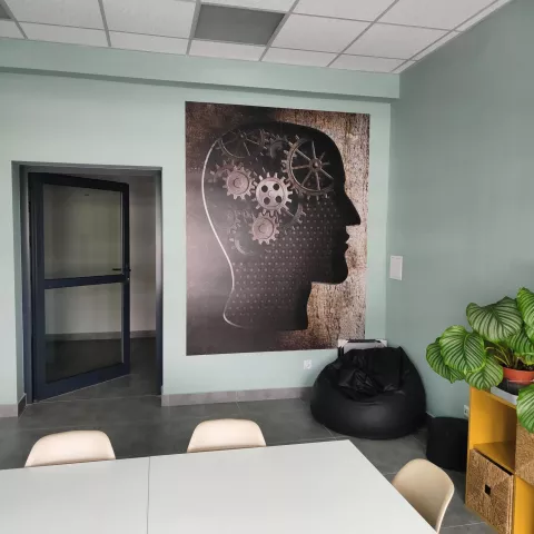 A room next to the drawing room in building A22 intended for students to relax with a table, chairs, a pouffe and a graphic on the wall depicting a mechanical head