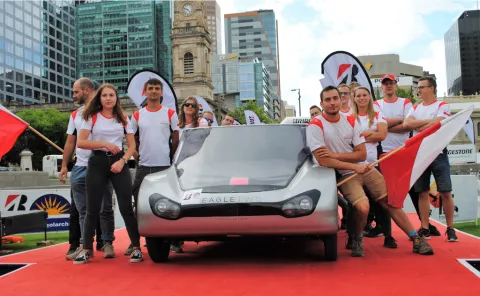 Grupa studentów z Koła Naukowego Lodz Solar Team stojących za pojazdem na energię słoneczną  na podium podczas zawodów 