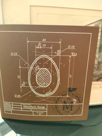 Karta świąteczna w kolorze brązowym na tle grafiki budynku Wydziału Mechanicznego PŁ