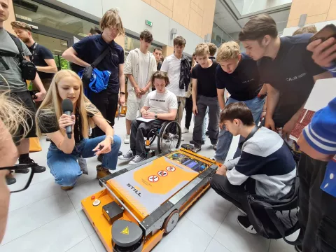 Grupa uczniów z prowadzącą pokaz maszyny mobilnej firmy STILL w patio Fabryki Inżynierów XXI w.