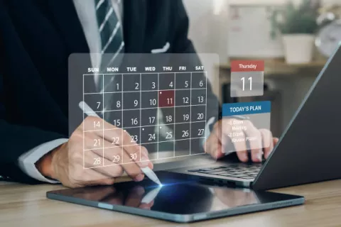 Grafika przedstawia mężczyznę przy laptopie planującego spotkania w kalendarzu